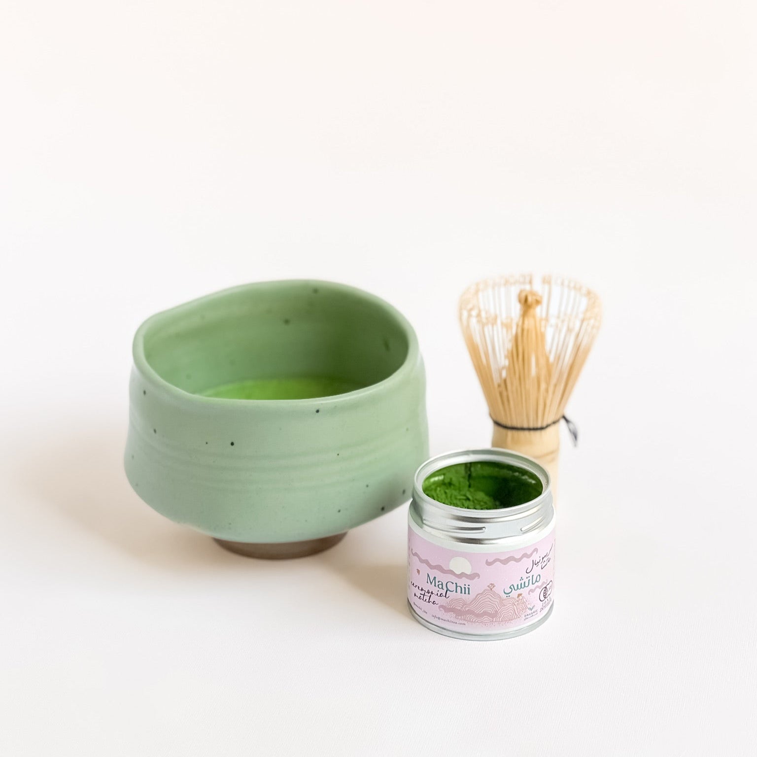 a ceremonial matcha tin opened next to a big handmade bowl of matcha. the whisk is laying on the table next to it. 